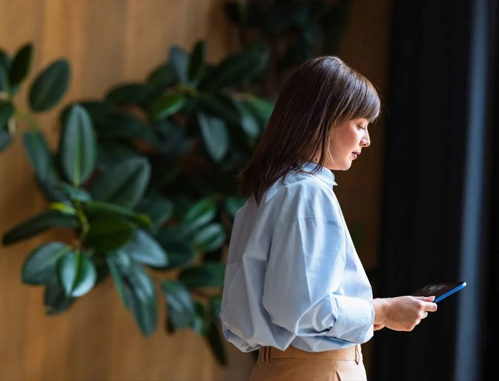 Woman checking her smartphone beside indoor plants.
