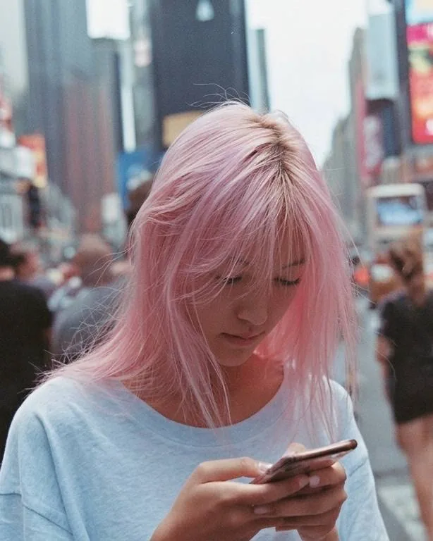 Person with pink hair checking a smartphone on a city street.