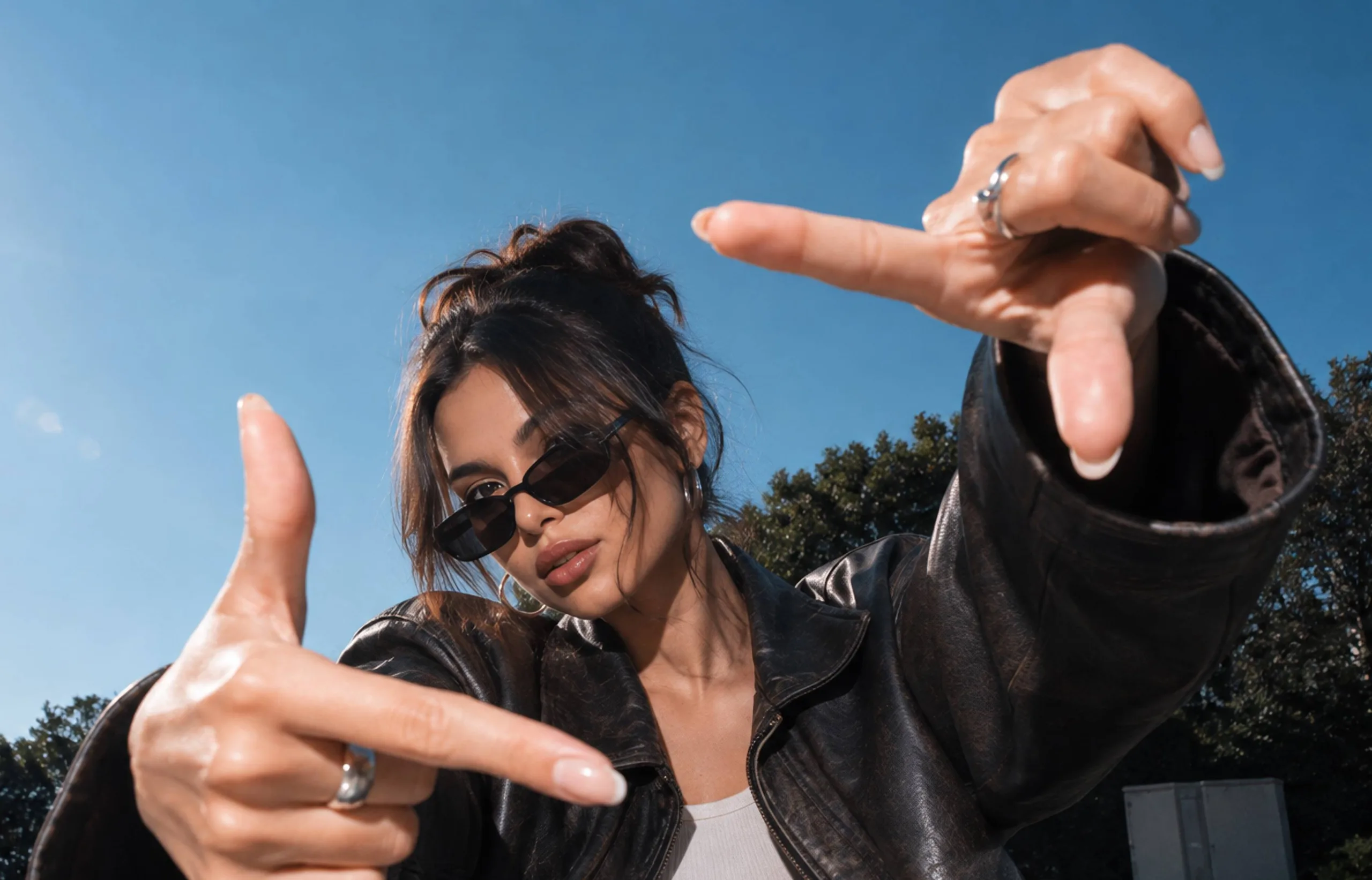 Woman in sunglasses framing a shot with her hands outdoors.
