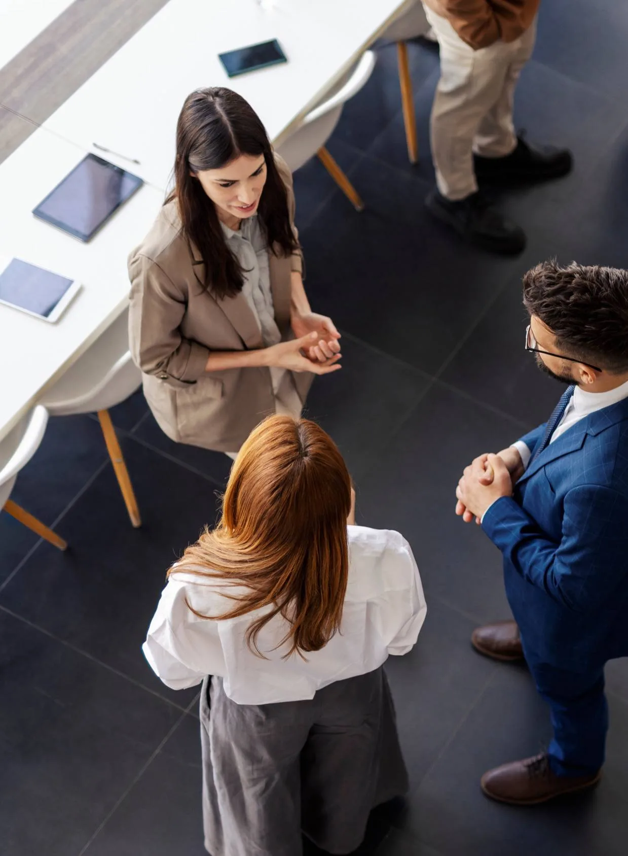 Overhead view of three people talking beside a meeting table.