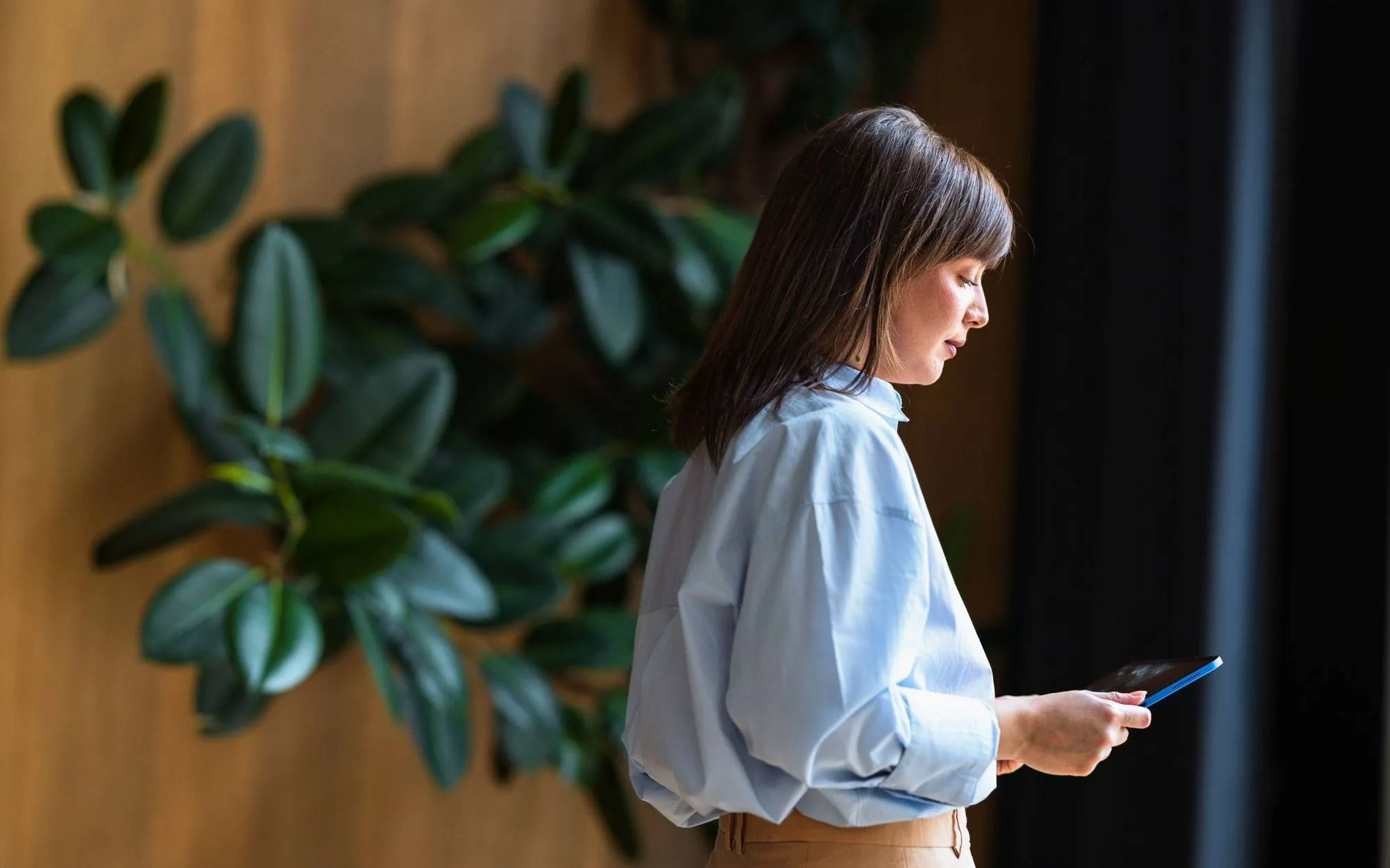 Woman checking her smartphone beside indoor plants.