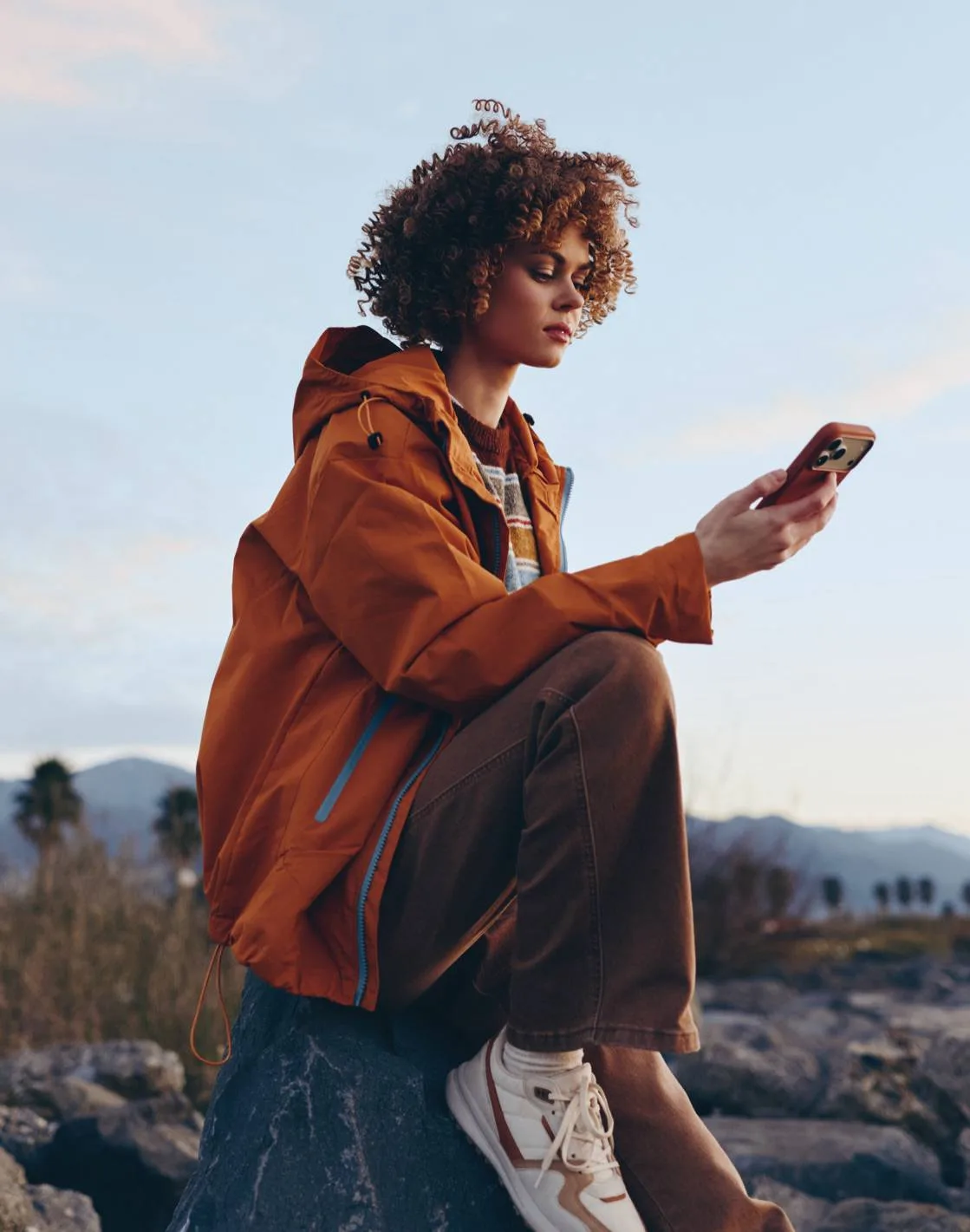 Person in an orange jacket checking a smartphone outdoors.