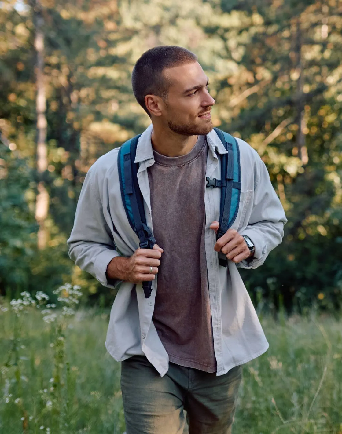 Man wearing a backpack walking along a wooded trail.